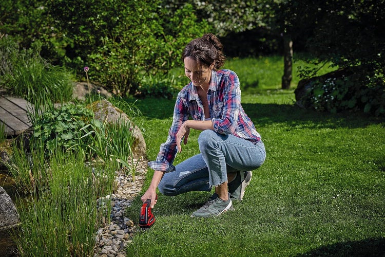 Eine Frau benutzt eine Akku-Grasschere, um die Rasenkante an einem Gartenteich zu schneiden.
