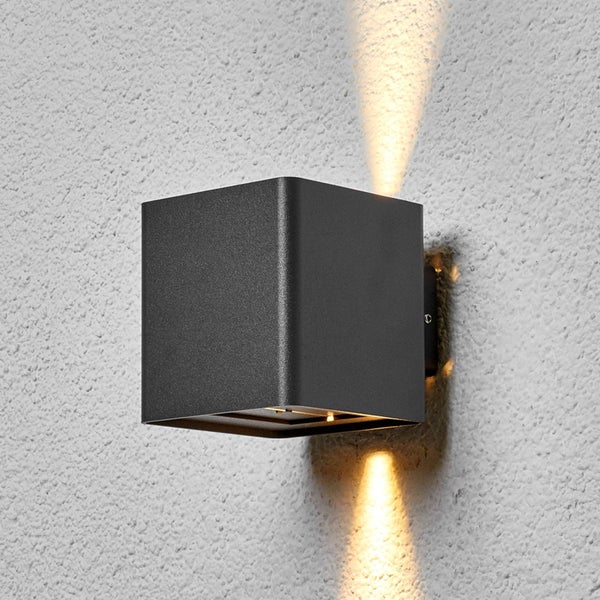 Würfelförmige Außenwandleuchte aus Metall mit Lichtaustritt nach oben und unten an einer Wand.