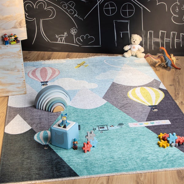 Kinderspielteppich mit Bergmotiv und Heißluftballons im Kinderzimmer mit Spielzeug und Kreidetafelwand im Hintergrund
