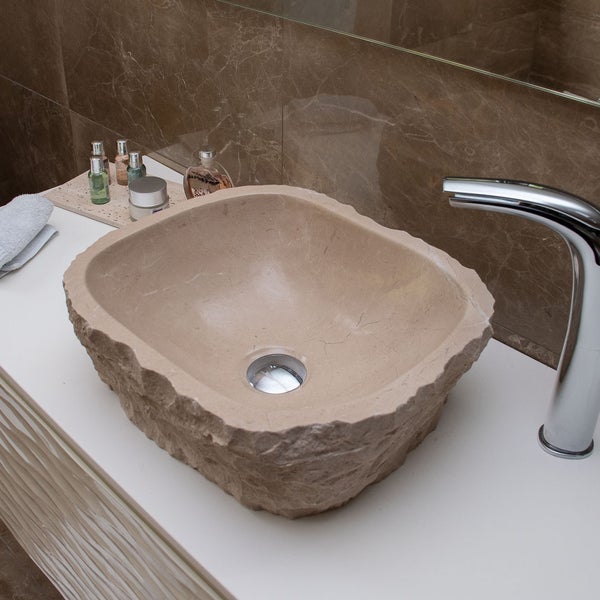 Aufsatzwaschbecken aus Naturstein mit bruchrauer Außenseite auf einer weißen Konsole mit verchromter Armatur im modernen Badezimmer.