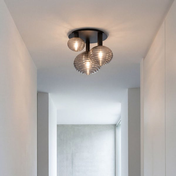 Dreiflammige Deckenleuchte mit geriffelten Glasschirmen in einem hellen, modernen Flur mit weißen Wänden und Betonakzent.