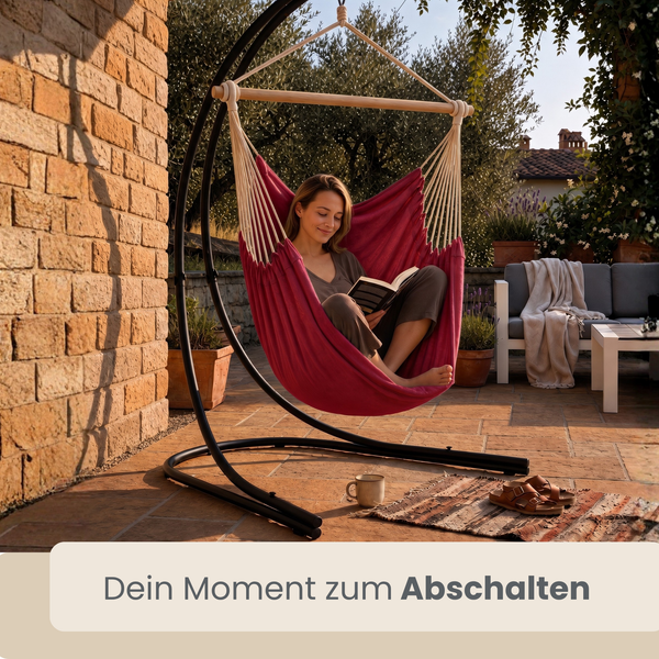 Frau liest ein Buch in einem Hängesessel mit Metallgestell auf einer Terrasse.