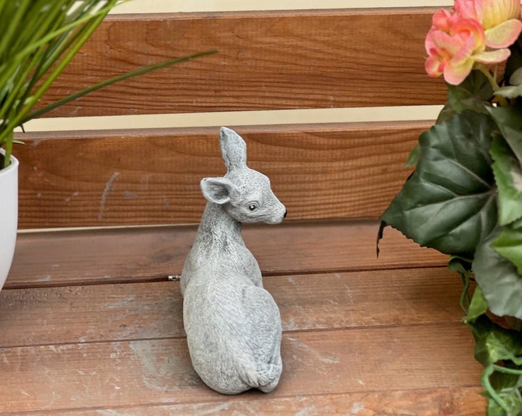 Gartenfigur liegendes Reh in Steinoptik auf einer Holzbank zur Dekoration im Außenbereich.