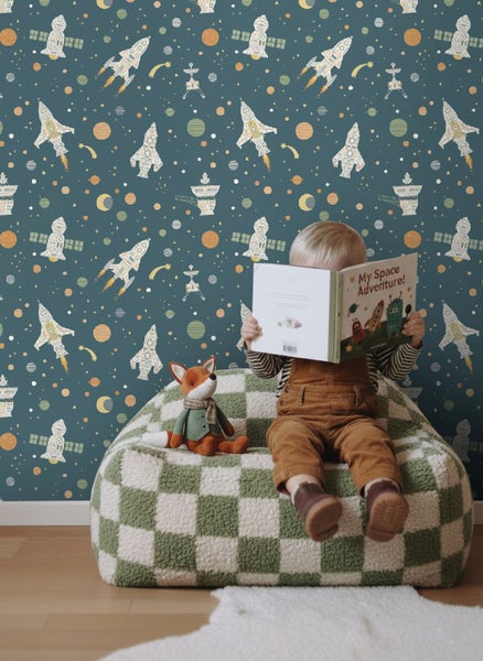 Vliestapete für das Kinderzimmer mit Weltraum-Motiven wie Raketen und Planeten. Ein Kind liest davor ein Buch auf einem Sitzsack.