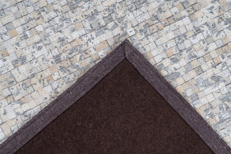 Detailaufnahme eines Teppichs mit gewebter Patchwork-Oberfläche und dunkler Filzrückseite mit Stoffeinfassung.