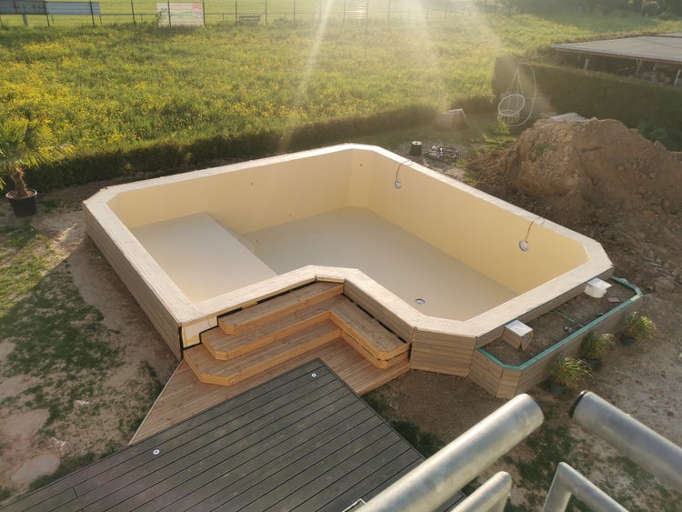 Moderner L-förmiger Swimmingpool im Bau im Garten mit Holztreppe und dunkler Terrasse.