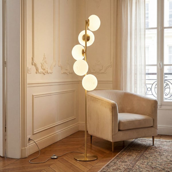Stehleuchte mit fünf geriffelten Glaskugeln und goldfarbenem Metallgestell in einem hellen Wohnzimmer mit Samtsessel und Parkettboden.