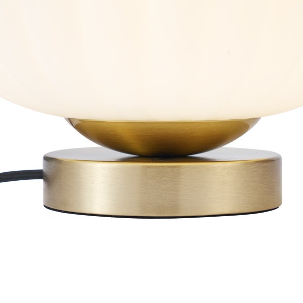 Detailaufnahme einer Tischleuchte mit einem runden Metallsockel in Messing gebürstet und einem weißen Schirm aus Glas.