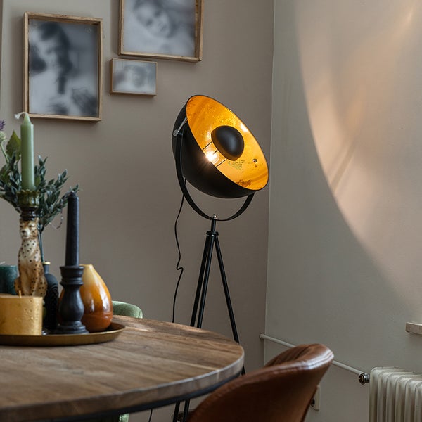 Stehleuchte mit Stativfuß, schwarzem Schirm und goldfarbener Innenseite in einem Wohnzimmer.