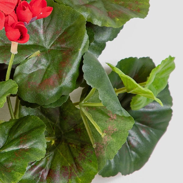 Künstliche Geranie mit grünen Blättern und roten Blüten in der Detailansicht.