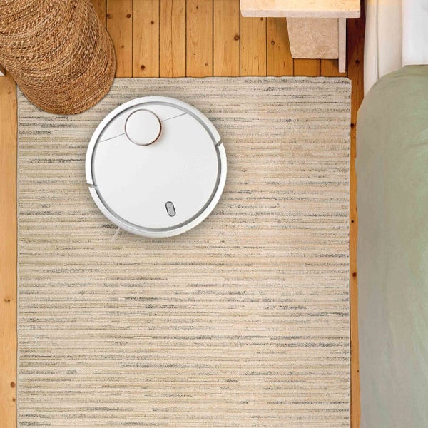 Saugroboter auf einem Teppich in einem Raum mit Holzboden und Korb