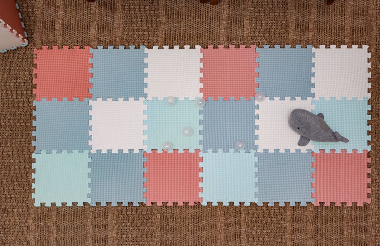Weiche Spielmatte aus bunten Schaumstoff-Puzzleteilen auf einem strukturierten Teppich mit einem Plüschwal und kleinen Bällen.