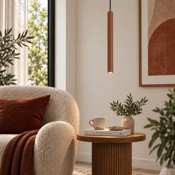 Moderne zylindrische Pendelleuchte in einem gemütlichen Wohnzimmer mit strukturiertem Sessel und Beistelltisch.