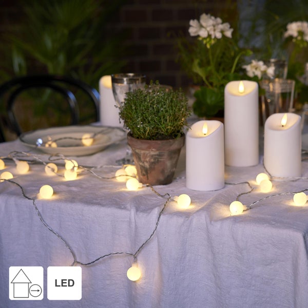 Dekorierter Tisch mit Pflanzen, Kerzen und einer LED-Lichterkette mit Kugeln