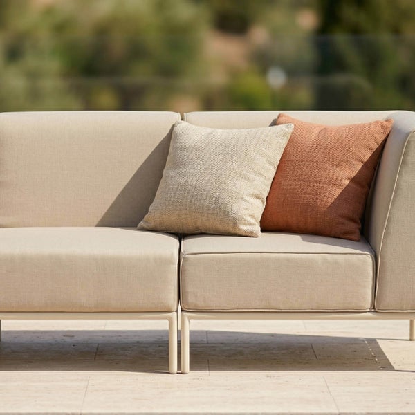 Modernes Outdoor-Lounge-Sofa mit hellem Textilbezug und Dekokissen auf einer Terrasse.
