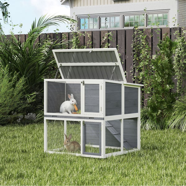 Zweistöckiger Kaninchenstall aus Holz mit klappbarem Dach, Rampe und Drahtgittertüren im Garten auf einer Rasenfläche.