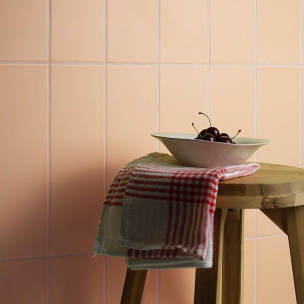 Wandfliesen im Rechteckformat verlegt vor einem Holzhocker mit einer Schale Kirschen und einem Geschirrtuch als dekoratives Arrangement