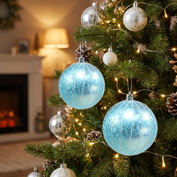 Weihnachtsbaum geschmückt mit glänzenden Christbaumkugeln und Lichterkette in einem wohnlichen Raum mit Kamin.