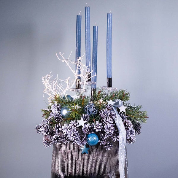 Adventskranz mit blauen Kerzen, Tannenzweigen, Kugeln und Sternen in silberfarbenem Gefäß.