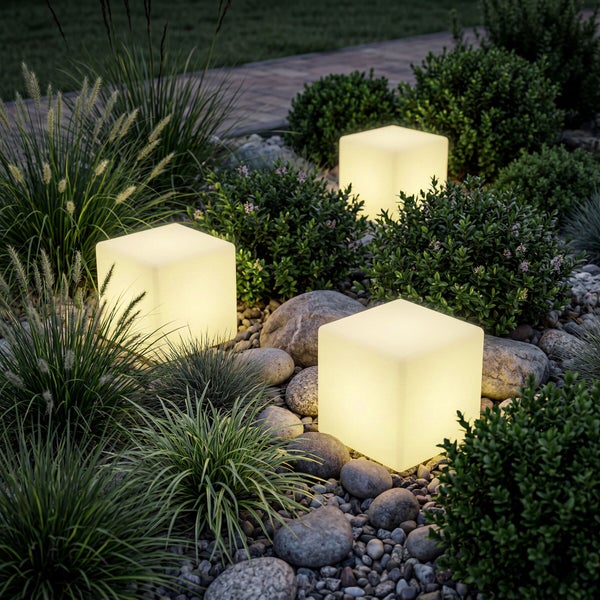 Drei beleuchtete Gartenwürfel in einem Beet mit Ziergräsern, Feldsteinen und niedrigen Sträuchern.