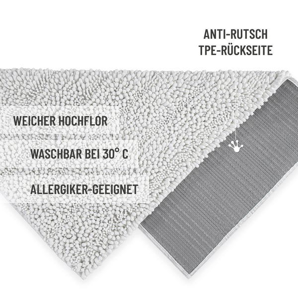 Weißer Badeteppich mit Mikrofaser-Noppen auf grauen Fliesen in einem hellen, organisierten Badezimmer mit geflochtenen Körben.