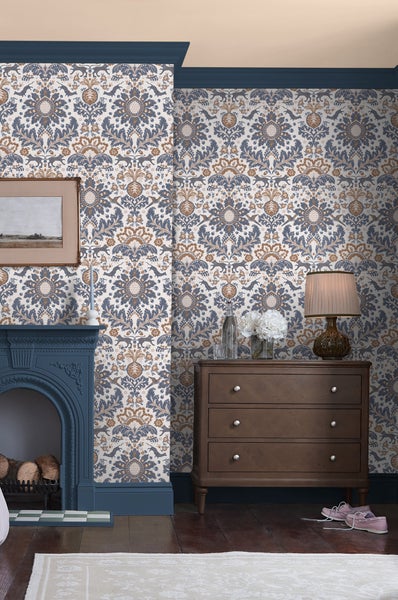 Vliestapete mit klassischem Damastmuster in Blau und Braun, stilvoll kombiniert mit Kamin und Holzkommode in einem eleganten Wohnzimmer.
