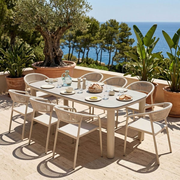 Modernes Gartenmöbel-Set mit ovalem Tisch und acht Seilgeflecht-Stühlen auf einer hellen Terrasse mit Meerblick.
