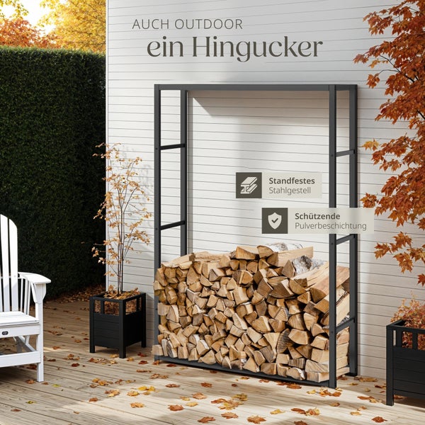 Schwarzes Kaminholzregal aus pulverbeschichtetem Stahl auf einer Holzterrasse vor einer weißen Wand, gefüllt mit Brennholz.