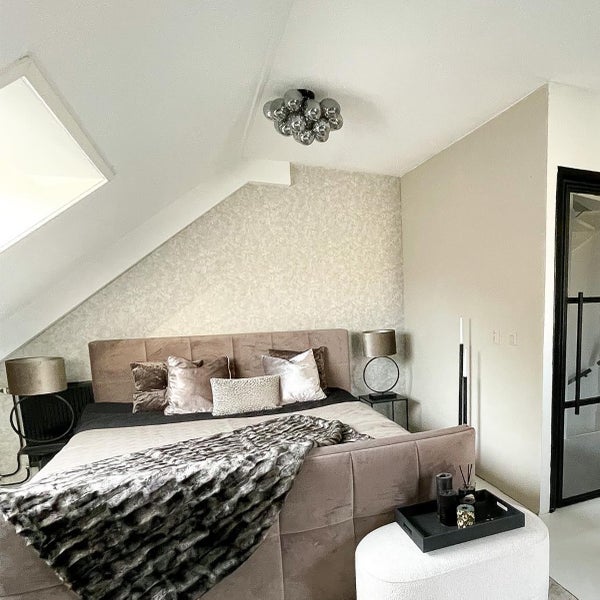 Schlafzimmer mit Bett, Kissen, Decke, Lampen, Beistelltischen und Dekoration unter einer Deckenleuchte