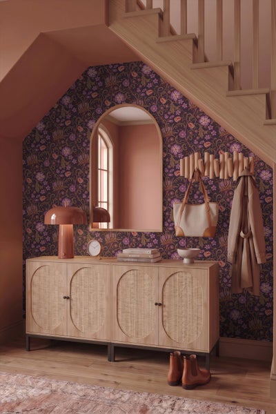 Moderner Flur unter einer Treppe mit Blumentapete, Rundbogenspiegel sowie Sideboard mit Rattantüren und Pilzlampe.