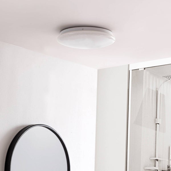 Runde weiße Deckenleuchte montiert an einer weißen Decke in einem hellen Badezimmer mit Spiegel und Dusche.