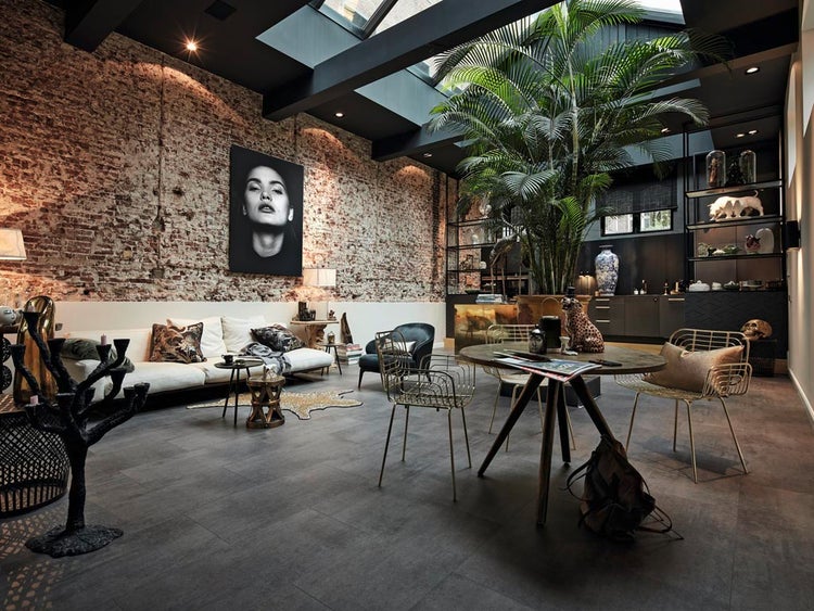 Offenes Wohnzimmer im Loftstil mit Ziegelwand, grauen Bodenfliesen, moderner Einrichtung, hohen Decken mit Oberlicht und einer grossen Palme.