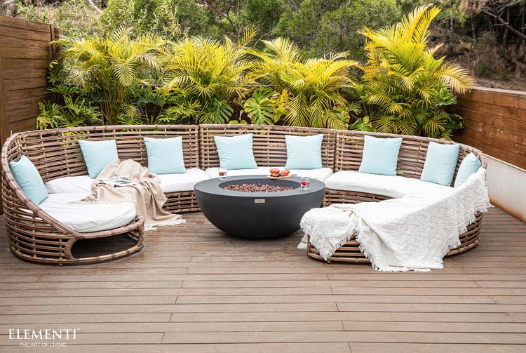 Organisierte Garten-Lounge aus Polyrattan mit hellen Polstern und zentraler Gaskaminstelle auf einer Holzterrasse mit Pflanzen. Elementi Logo.