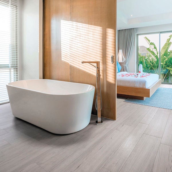 Freistehende Badewanne vor einer Holzwand mit freistehender Armatur in einem offen gestalteten Badezimmer und angrenzendem Schlafzimmer.