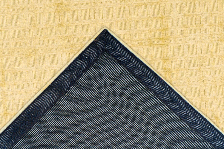 Nahaufnahme einer Teppichecke mit beige strukturierter Oberfläche und dunkelblauer Gitterrückseite.
