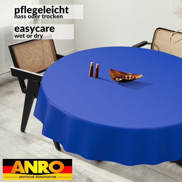 Runde blaue Tischdecke auf einem Esstisch in einem hellen Raum, minimalistisch, Stühle mit Geflecht, pflegeleicht nass oder trocken, Anro Logo.