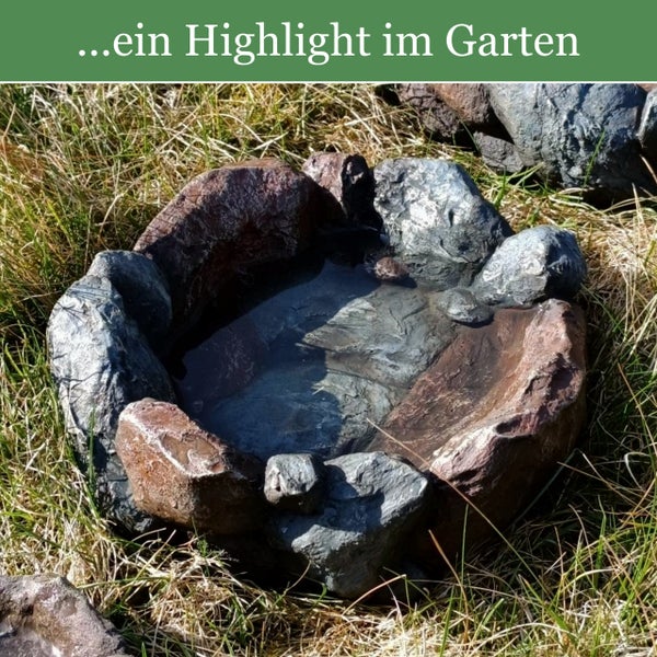 Dekorativer Gartenteich in Steinoptik auf einer Grasfläche, gefüllt mit Wasser.