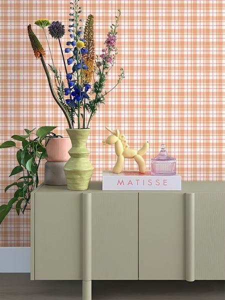 Dekoratives Sideboard mit Blumenstrauß, Zimmerpflanze und Zierobjekten vor gemusterter Tapete