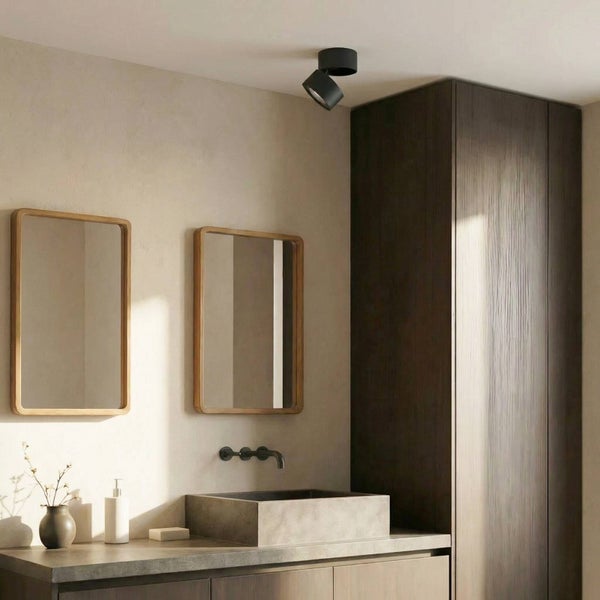 Modernes Badezimmer mit Steinwaschbecken, dunklen Holzschränken, zwei Spiegeln mit Holzrahmen und einem verstellbaren schwarzen Deckenstrahler.
