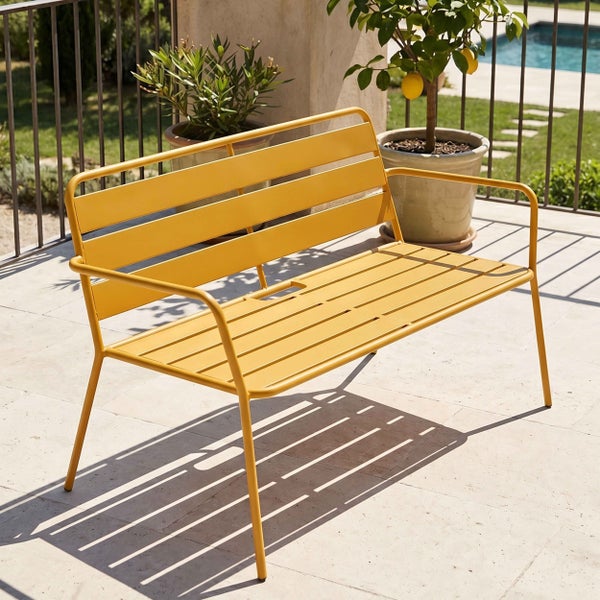 Gelbe Gartenbank aus Metall mit Lattenstruktur auf einer hellen Terrasse neben Pflanzen und einem Pool im Hintergrund.