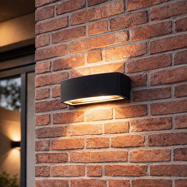 Moderne Außenwandleuchte in Schwarz mit Lichtaustritt nach oben und unten an einer Ziegelwand.
