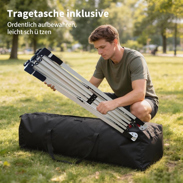 Ein Mann verstaut ein zusammengeklapptes Pavillongestell aus Metall in einer großen schwarzen Tragetasche auf einer Wiese.