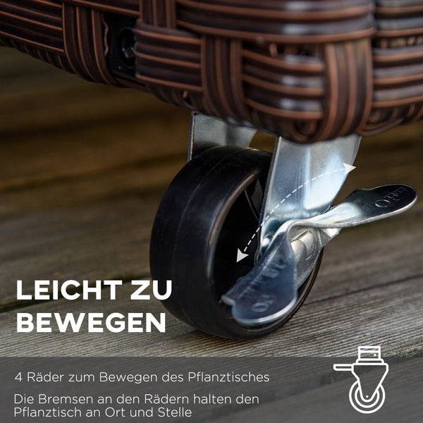 Brauner Pflanzkasten aus Rattan mit Blumen und Gartengeräten vor einer Steinmauer