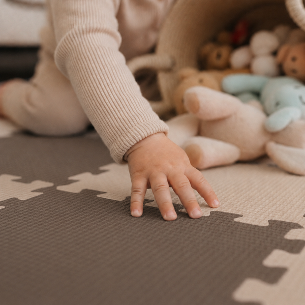 Ein Kleinkind sitzt auf einer Puzzlematte mit weichen Stofftieren in einem Korb.