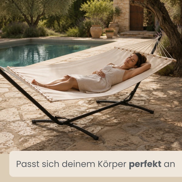 Helle Stabhängematte mit dunklem Metallgestell auf einer Steinterrasse neben einem Pool, in der eine Frau liegt.