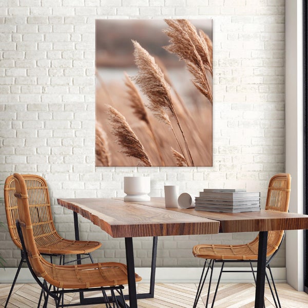 Wandbild mit Schilfmotiv über einem Holztisch mit Rattanstühlen vor einer weiß gestrichenen Ziegelwand.