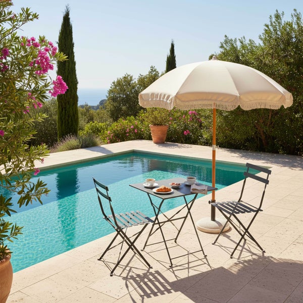 Bistro-Set bestehend aus quadratischem Metalltisch und zwei Klappstühlen neben einem Pool unter einem Fransensonnenschirm auf einer Terrasse.