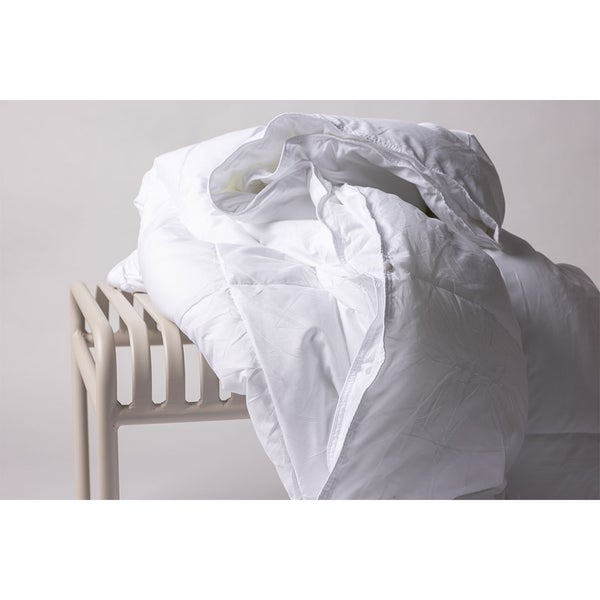 Weiße Steppdecke drapiert über einen modernen Metallhocker, weiches Material, Bettwaren für das Schlafzimmer.