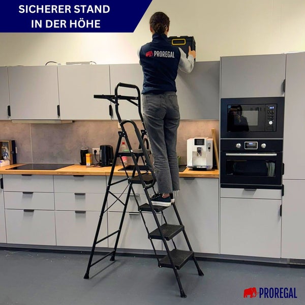 Frau steht auf einer Trittleiter in einer Küche und hält einen Werkzeugkasten.