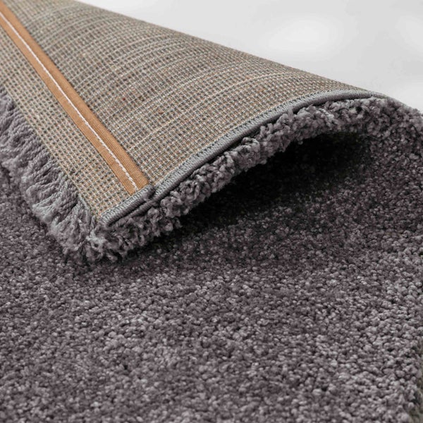 Detailansicht eines Hochflor-Teppichs mit umgeschlagener Ecke, die den gewebten Rücken und die dichte Faserstruktur zeigt.